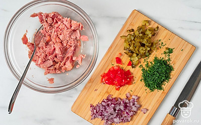 Выложите указанное в рецепте количество тунца в миску, разомните вилкой. Мелко нарежьте лук, маринованный огурец, помидор и укроп.