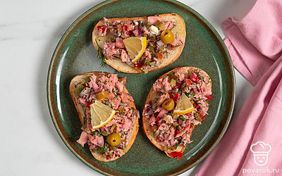 Украсьте закуску с тунцом половинками оливок и ломтиками лимона.