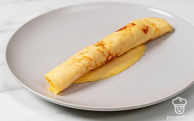Аккуратно сверните омлет в рулетик. Точно так же приготовьте оставшуюся часть закуски.
