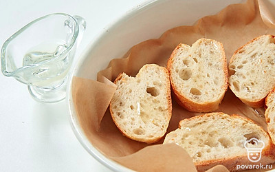 Смажьте ломтики багета маслом, выложите на противень и уберите в духовку на 10 минут. Через 5 минут переверните хлеб на другую сторону.