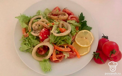 На плоскую тарелку выложите несколько ложек готового салата. Посыпьте салат с кальмарами мелко нарезанной зеленью и итальянскими травами. Украсьте подачу салата дольками лимона и целыми помидорами черри.