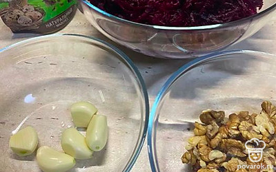 Пока варится свёкла, почистить и раздавить в чеснокодавилке чеснок, размельчить, но не сильно, грецкие орехи. Натереть варёную свёклу на крупной тёрке. 