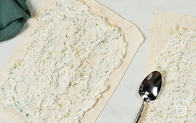 Разрежьте листы лаваша на 2 части. На каждый прямоугольник выложите по несколько ложек начинки. Распределите ее по всей поверхности лаваша, слегка отступая от краев.