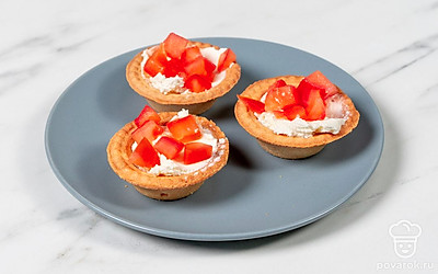 Положите в каждую тарталетку примерно по 1 ч. л. сыра фета. Сверху распределите кубики помидора.