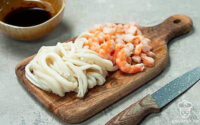 Сварите кальмары и креветки. Доведите воду в кастрюле до кипения. Затем посолите и опускайте в воду по одному кальмару на 15 секунд. Остудите их и нарежьте кольцами. В другую кастрюлю наберите воду, посолите и поставьте на средний огонь. В кипящую воду положите креветки и варите около 5 минут. Затем остудите их, очистите и нарежьте, отложив три креветки для подачи.