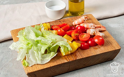 Приготовьте ингредиенты для салата. Отварите креветки в подсоленной воде. Остудите и очистите. Листья салата нарвите руками. Болгарский перец нарежьте крупными кубиками. Томаты черри поделите пополам. С кукурузы и оливок слейте жидкость и переложите их в отдельную миску.