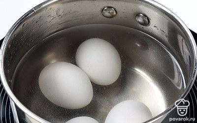 Выложите в сотейник и залейте водой яйца. Поставьте их на максимальный огонь. Доведите воду до кипения, а затем убавьте нагрев до минимума. Варите яйца до готовности в течение 7-10 минут, а после этого остудите.