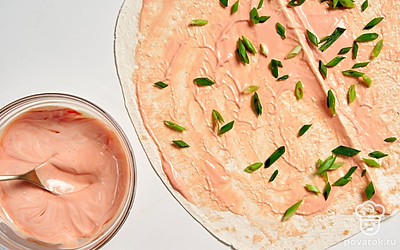 Разверните лист лаваша. Равномерно смажьте его третью соуса. Посыпьте измельченным зеленым луком.