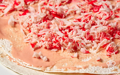 Сверху положите второй лист лаваша. Также тонко смажьте его половиной оставшегося соуса и распределите крабовые палочки.