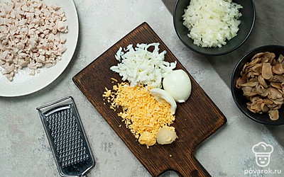 Подготовьте ингредиенты. В емкость с измельченным куриным филе натрите желтки на средней терке. Сюда же добавьте 2 ст. л. майонеза, соль и перемешайте. Получившуюся массу разделите на две части прямо внутри емкости. На крупной терке натрите яичные белки, консервированные шампиньоны нарежьте на тонкие ломтики. Смешайте ингредиенты и по аналогии массу разделите пополам.