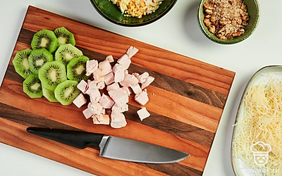 Измельчите продукты. Порежьте куриную грудку маленькими кубиками, киви — небольшими кусочками. Измельчите грецкие орехи. Яйца и сыр по отдельности натрите на терке с крупными ячейками.