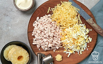 Подготовьте ингредиенты для салата. Куриное филе нарежьте на небольшие кусочки. Яйца измельчите. С ананасов слейте жидкость, нарубите их кубиками. Сыр натрите на крупной терке. Чеснок продавите в чеснокодавке. Грецкий орех поделите на половинки.