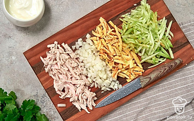 Подготовьте ингредиенты. Куриное филе нарежьте небольшой по размеру соломкой. То же повторите с яичными блинами. Огурцы очистите от кожуры, а после нарежьте их брусочками. Мелко порежьте петрушку.