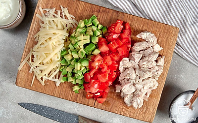 Подготовьте ингредиенты. Авокадо нарежьте маленькими кубиками, сбрызните лимонным соком. Куриное филе отварите до готовности, остудите и разберите на волокна. Сыр натрите на крупной терке. Помидор мелко порежьте.