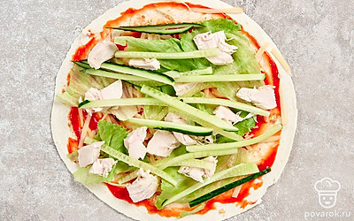 На рабочую поверхность стола положите лист лаваша и смажьте кетчупом. Распределите по лавашу сыр. Сверху разложите салат. Остывшее филе нарежьте на кусочки и выложите поверх листьев салата. Далее положите нарезанный огурец.