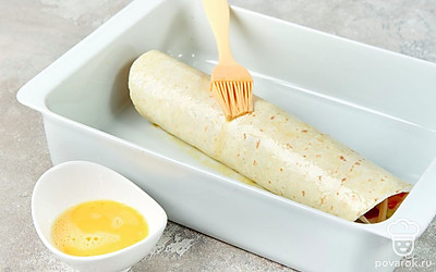 Закрутите лаваш с начинкой в рулет. Взбейте вилкой яйцо и смажьте им рулет. Переложите тортилью на противень и отправьте в духовку на 15 минут.