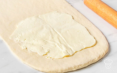 Достаньте охлажденное тесто. Раскатайте на рабочей поверхности в прямоугольник небольшой толщины. Сверху выложите пласт масла с пергамента так, чтобы он занимал примерно 3/4 площади теста с одной стороны.
