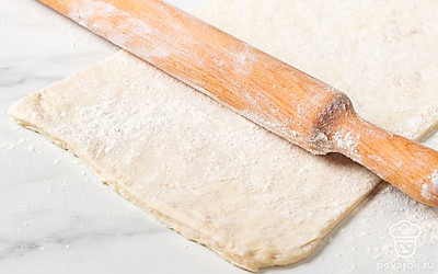 Припылите стол мукой. Выложите готовое слоеное тесто. Раскатайте в тонкий прямоугольный пласт.