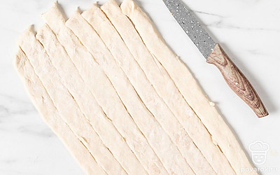 Нарежьте пласт на 7 полосок шириной примерно 2 см. Если у вас есть круглый нож для пиццы, то нарезать им будет удобнее. 