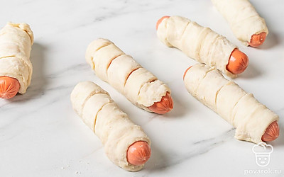 Поставьте духовку разогреваться на 180 ℃. Возьмите сосиску и обмотайте ее полоской теста, слегка накладывая завитки друг на друга. Сделайте то же самое с остальными сосисками и полосками теста.