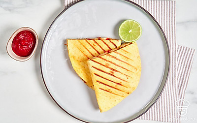 Разрежьте мексиканскую лепешку пополам и выложите на тарелку для подачи. Дополните блюдо дольками лайма и пиалой с томатным соусом.