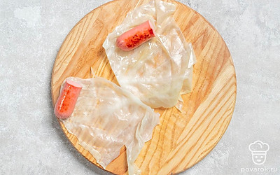 На край капустного листа положите половину сосиски.