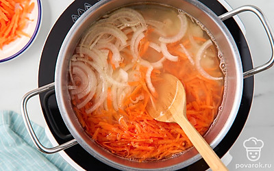 Налейте воду в кастрюлю, поставьте на средний огонь и доведите до кипения. Выложите обжаренный лук с мукой в кастрюлю с закипевшей водой. Добавьте туда оставшийся сырой лук и сырую тертую морковь, все перемешайте.