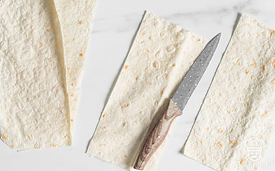 Разрежьте лист лаваша на 4-5 полосок шириной примерно 9-10 см и длиной 40-50 см. Тоньше резать не стоит, иначе начинку будет трудно заворачивать. Для нарезки используйте обычный нож или круглый нож для пиццы.