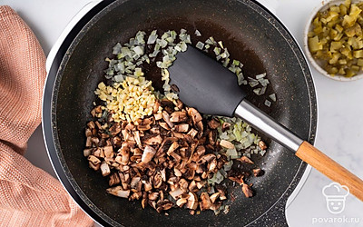 Добавьте к луку грибы, огурцы и чеснок. Перемешайте. Готовьте еще 5-7 минут, периодически помешивая.