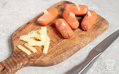 Сыр нарежьте на маленькие тонкие кусочки. В каждой сосиске сделайте несколько надрезов и вложите в них сыр.