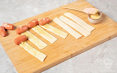 Смажьте получившиеся прямоугольники горчицей. Положите на каждый по сосиске так, чтобы края немного выходили наружу.