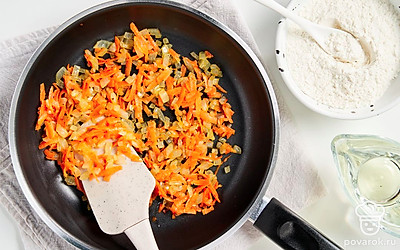 Приготовьте овощную зажарку. В широкой плоской сковороде соедините подсолнечное и сливочное масло, разогрейте. Добавьте измельченный лук, обжарьте 2-3 минуты. Выложите тертую морковь, готовьте при постоянном помешивании около 2-3 минут. Введите муку. Не забывая помешивать, жарьте 1,5-2 минуты.