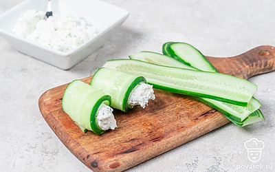 Смешайте творог с укропом и йогуртом. Посолите и перемешайте. Выложите немного начинки на слайс огурца и сверните рулетиком. 