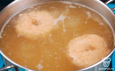 В кипящую воду опустите круглые заготовки по очереди. Как только бейгл всплывет, отсчитайте 3-4 секунды и достаньте при помощи шумовки. Стряхните лишнюю воду и выложите на противень, застреленный бумагой для выпечки. Таким образом сварите все заготовки. Выпечка после такой процедуры будет более пористой, а корочка сверху — румяной и хрустящей.