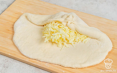 Натрите сулугуни на крупной терке и разбейте в него яйцо. Достаньте готовое тесто из золодильника, раскатайте в пласт толщиной 1 см. Распределите начинку, не доходя до краев 2-3 см. Соберите края теста сверху по центру, залепите и переверните. Раскатайте еще раз.