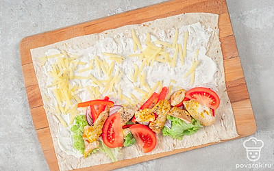 Разверните лаваш и разложите на рабочей поверхности, смажьте его соусом. Посыпьте лаваш тертым сыром. На одной из сторон лаваша выложите немного салатных листьев, овощей и куриного филе. После этого аккуратно сверните лаваш в плотный рулет. Повторите действия с остальными ингредиентами.