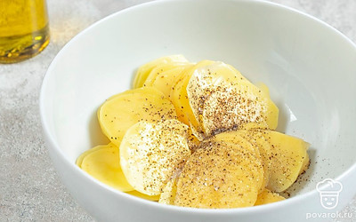 Нарежьте очищенный картофель тонкими ломтиками, выложите на бумажные полотенца, чтобы избавиться от лишнего сока. Переложите картофельные ломтики в миску, добавьте к ним масло, соль и перец и хорошо перемешайте.