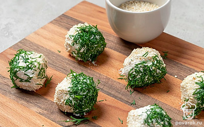 Доведите закуску до готовности. Укроп и кунжут выложите по плоским мискам. Половину заготовок щедро обваляйте в зелени, вторую — в кунжуте. Переместите их обратно на деревянную доску и отправьте охлаждаться на 30 минут.