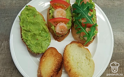 Намажьте полученной смесью ломтики багета, выложите сверху нарезанный помидор и креветки. Украсьте листьями руколы, сбрызните оливковым маслом и подавайте.