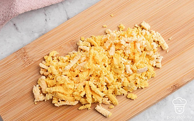 Аккуратно очистите яйца от скорлупы, а затем каждое разрежьте вдоль на две части. Удалите желтки и измельчите их, белки отложите в сторону ⎯ они понадобятся чуть позже.