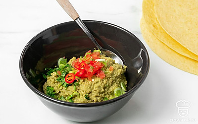 Приготовьте соус гуакамоле. В глубокой миске разомните авокадо с щепоткой соли, лаймовым соком, кинзой и чесноком. Затем добавьте к авокадо мелкие кубики помидора и перца халапеньо, нарезанный зеленый лук. Тщательно размешайте.