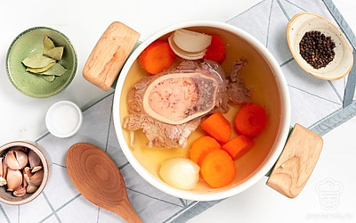 Отварите говяжью голень. В большую кастрюлю положите голень и налейте воду. После закипания снимите пену, положите луковицу и морковку. Если вода мутная, слейте ее, ополосните голень, залейте новой водой и дождитесь закипания. Установите маленький огонь, чтобы вода не бурлила, а слегка булькала. Варите 2 часа. Достаньте овощи и мясо, процедите отвар.