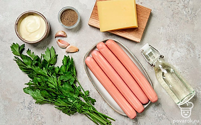 В каждой сосиске сделайте надрезы посередине вдоль. Сыр натрите на мелкой терке. Петрушку промойте, просушите и мелко порубите. Чеснок очистите и пропустите через пресс. Для подачи помидор и огурец помойте, обсушите и нарежьте дольками. Разогрейте духовку до 180 градусов.