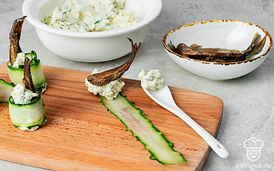 Приготовьте закуску. Огурец нарежьте тонкими слайсами, используя для этого овощечистку. Затем возьмите один овощной ломтик, выложите на него немного начинки, не доходя до края, а сверху положите рыбу хвостом вверх. Заверните закуску в рулет и поставьте на тарелку. Повторите действия со всеми ингредиентами.