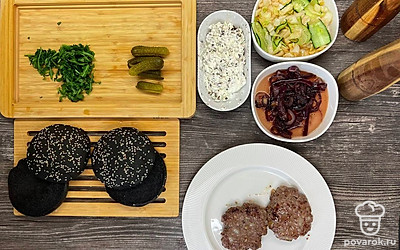 Руколу нарвите руками крупно. Маринованные огурцы нарежьте тонкими пластинами. Нижние и верхние половинки булочек смажьте трюфельным кремом. На нижние половинки булочек выложите половину руколы, маринованные огурчики, котлеты и карамелизованный лук, сверху выложите оставшуюся руколу и накройте верхними половинками булочек.