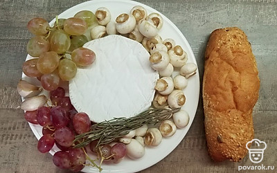 Камамбер освободите от упаковки, виноград и грибы вымойте и дайте стечь воде. Чеснок очистите и нарежьте тонкими пластинками, оборвите листики у розмарина. Приготовьте небольшую форму для запекания, смажьте ее оливковым маслом, включите духовку на 180 ºС.