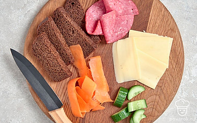 Подготовьте ингредиенты. Ломтик хлеба разрежьте на 4 небольших квадрата. Колбасу, сыр и огурец нарежьте тонкими ломтиками или полосками. Морковь нарежьте маленькими треугольниками.