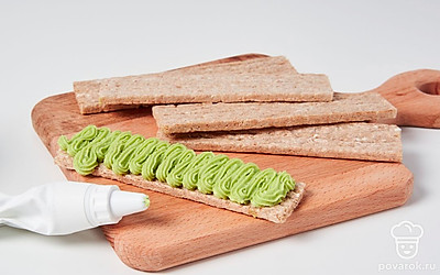 Приготовьте закуску. Переложите готовый соус в кондитерский мешок и выложите красиво на каждый хлебец, либо просто намажьте их соусом из авокадо.