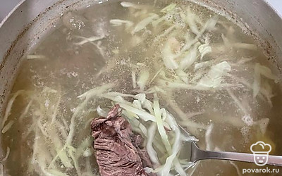 Мясо на кости достаем из бульона и режем на небольшие кусочки. Отправляем мясо обратно в кастрюлю.