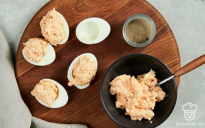 Приготовьте фаршированные яйца. Яйца разрежьте пополам вдоль. Положите в чашу блендера запеченного лосося, желтки, сливочный сыр и свежемолотый перец, хорошо измельчите. Полученную массу разложите на половинки яиц.